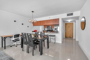 A modern kitchen with stainless steel appliances, a dining area with a glass table and black chairs, and a wooden door. - Chic City Condo With Pool & Gym (Miami)