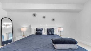 A bedroom with a large bed, two bedside lamps, a mirror, and decorative wall art. - Chic City Condo With Pool & Gym (Miami)