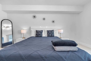 A bedroom with a large bed, two bedside lamps, a mirror, and decorative wall art. - Chic City Condo With Pool & Gym (Miami)