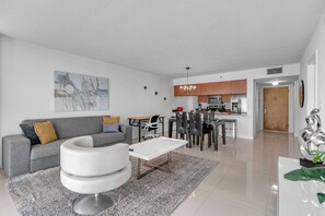 A modern living room with a grey sofa, a white coffee table, and a dining area with a kitchen in the background. - Chic City Condo With Pool & Gym (Miami)