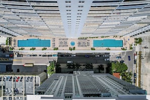 A high-rise building with multiple balconies, two swimming pools, and a parking area. - Chic City Condo With Pool & Gym (Miami)