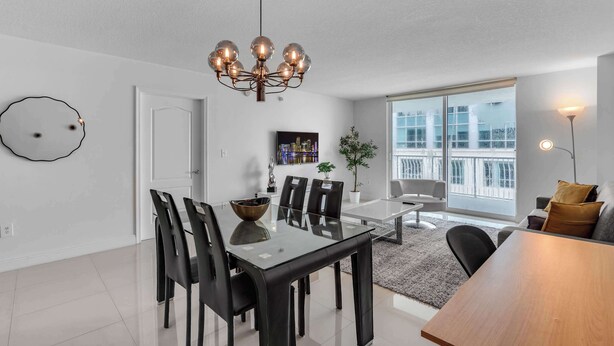 A modern living room with a dining area, large windows, and a chandelier. - Chic City Condo With Pool & Gym (Miami)