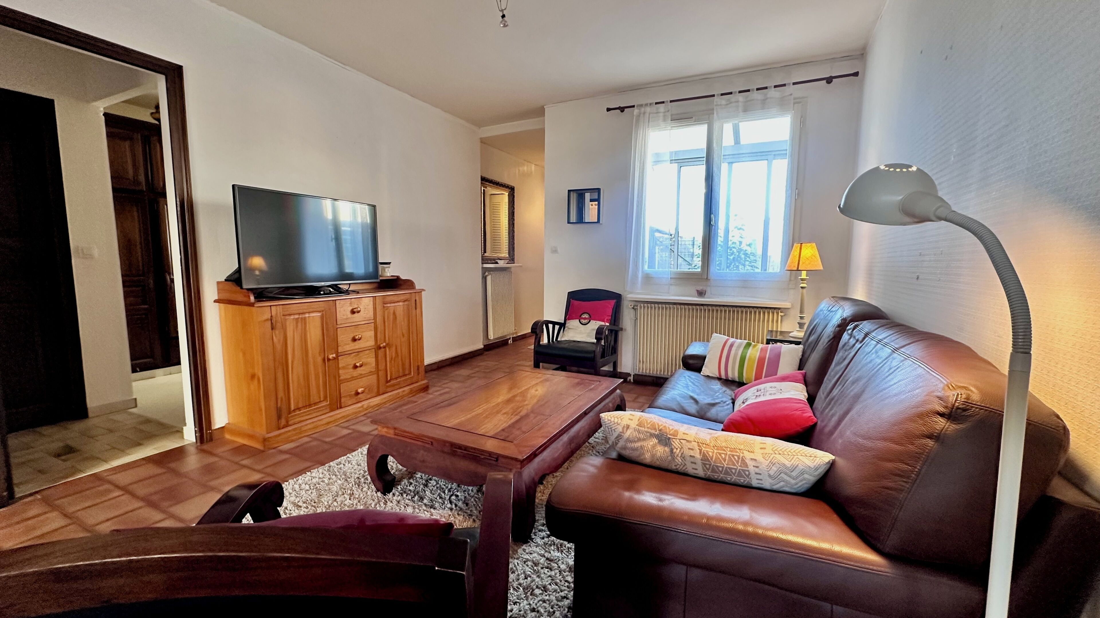 A living room with a television on a wooden cabinet, a leather sofa with cushions, a coffee table, and a lamp.