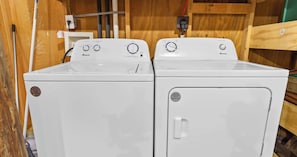 Two white front-loading washing machines with control knobs and a wooden cabinet in the background. - The Gothic House With Beachfront (Pensacola)