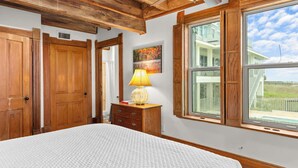 Une chambre avec un grand lit, une armoire en bois, une table de chevet avec une lampe et une fenêtre donnant sur une maison et le ciel.