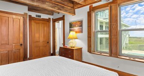 A bedroom with a large bed, wooden wardrobe, a nightstand with a lamp, and a window with a view of a house and sky. - The Gothic House With Beachfront (Pensacola)