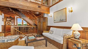 Un vaste espace de vie comprenant un escalier, un ensemble de canapés, une table basse et une petite table d’appoint en osier.