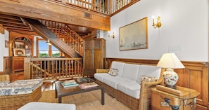 A spacious living area with a staircase, a sofa set, a coffee table, and a wicker side table. - The Gothic House With Beachfront (Pensacola)