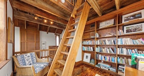 Une pièce chaleureuse avec une échelle en bois, un fauteuil en osier et une bibliothèque remplie de livres.
