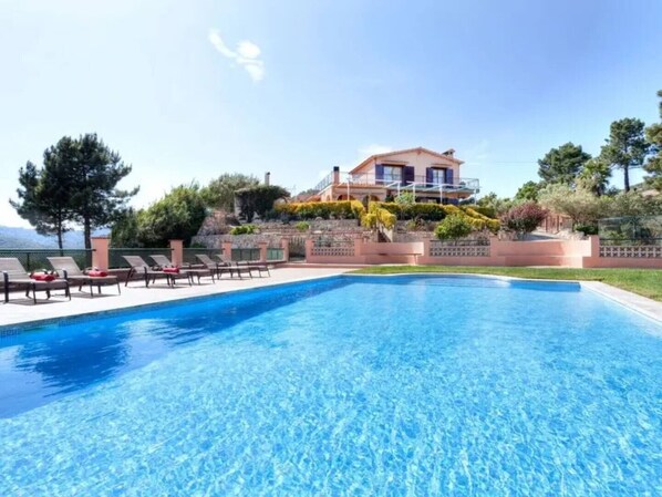 Une piscine aux eaux cristallines, avec des chaises longues et une maison en arrière-plan.