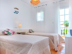 Ein Hotelzimmer mit zwei Betten, einem kleinen Tisch, einer Lampe, einer dekorativen Wanddekoration und einem Fenster mit Blick auf Grün.