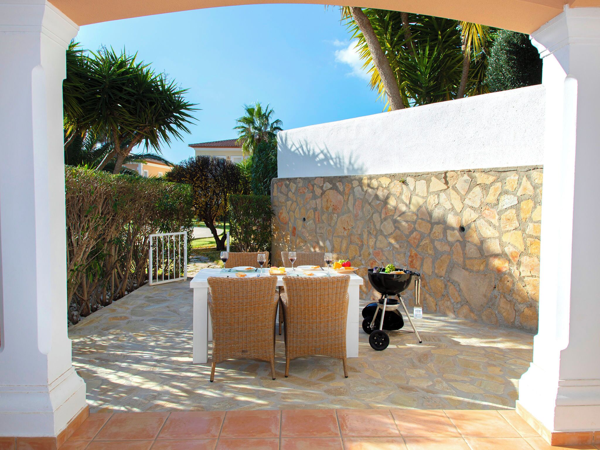 An outdoor patio with a stone wall, a table set for dining, and a grill.