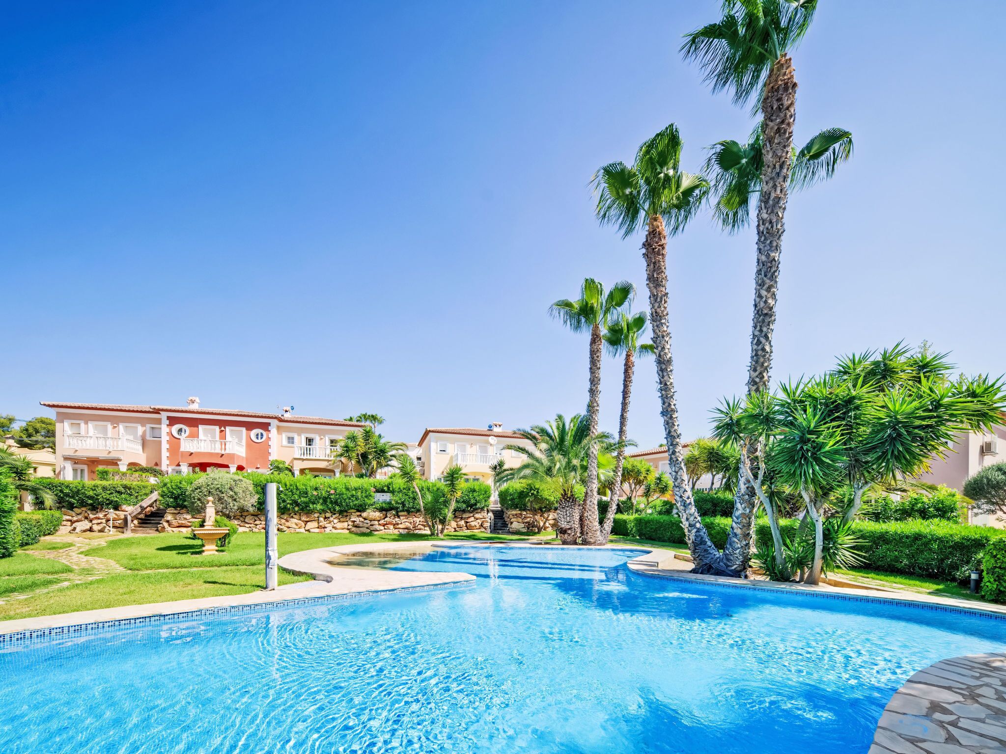 Una piscina rodeada de palmeras y un edificio con balcones.