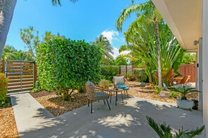 A patio with a seating area, a small table, and a variety of plants. - Ventur Escapade Heated Pool Guesthouse (Wilton Manors)