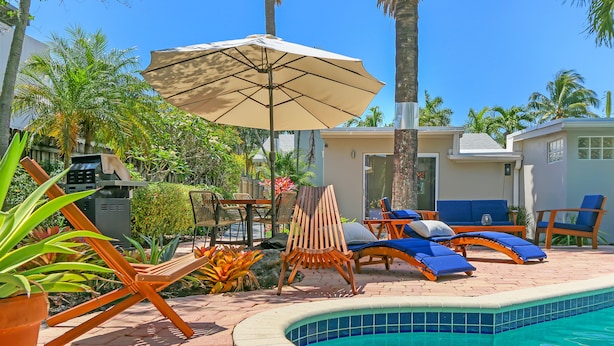 A poolside area with lounge chairs, a pool, and a covered seating area. - Ventur Escapade Heated Pool Guesthouse (Wilton Manors)