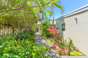 A narrow pathway flanked by lush greenery and a wooden fence, leading to a building with a window and a door. - Ventur Escapade Heated Pool Guesthouse (Wilton Manors)