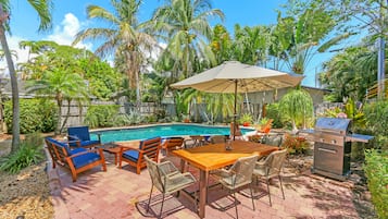 Um quintal com piscina, móveis de terraço e churrasqueira.