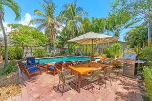 Um quintal com piscina, móveis de terraço e churrasqueira.