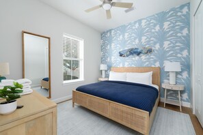 A bedroom with a bed, a bedside table, a lamp, a mirror, and a window with blinds. - Seashell Oasis - Heated Pool/Hot Tub/Putting Green/Walk to Beach (St. Augustine)