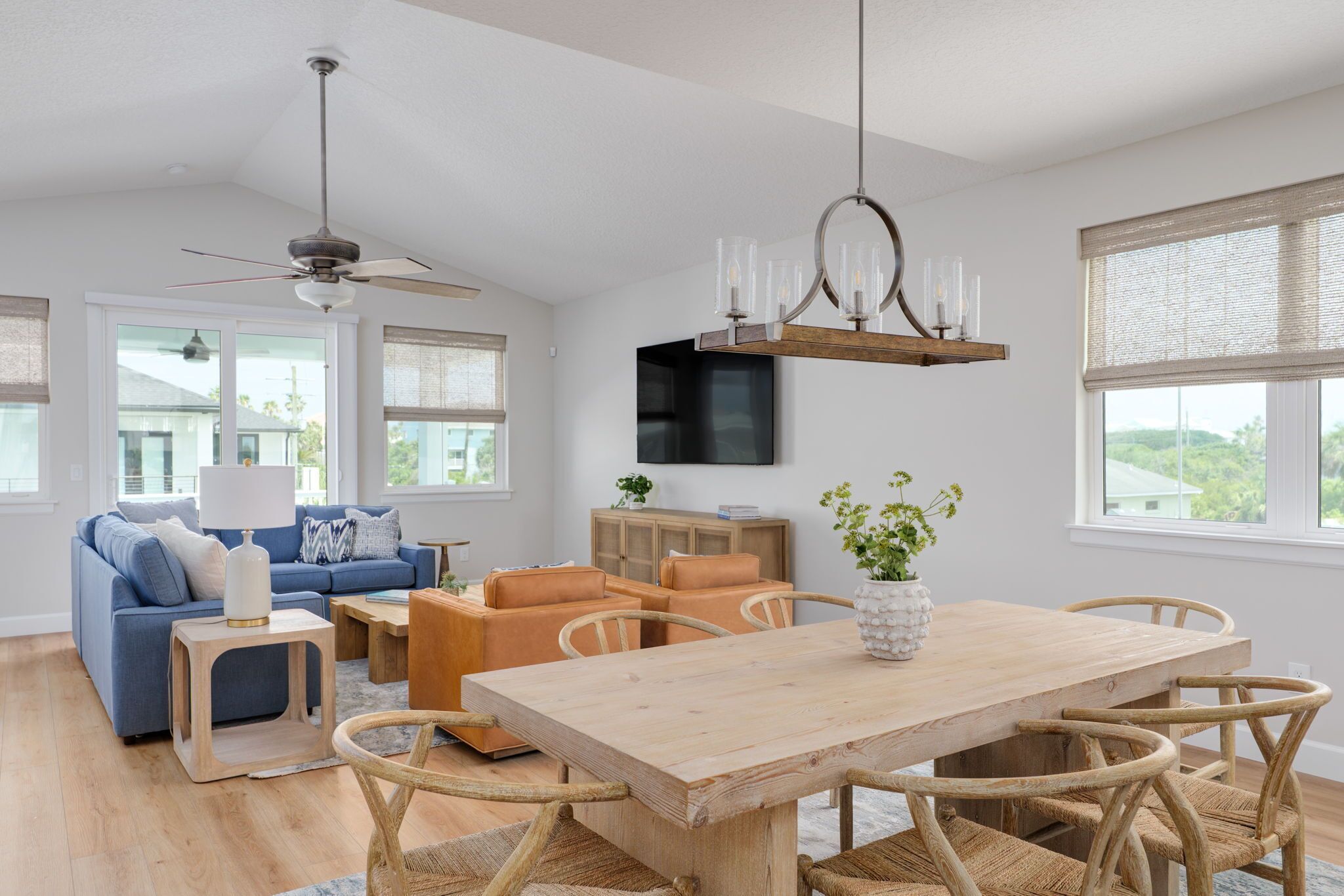 A modern living room with a blue sofa, orange chairs, a wooden dining table, and a ceiling fan.
