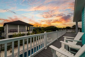 A deck with white railings overlooking a swimming pool and a house with a dark roof. - Seashell Oasis - Heated Pool/Hot Tub/Putting Green/Walk to Beach (St. Augustine)