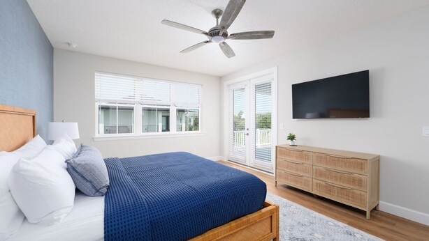 Ein Schlafzimmer mit einem Bett, einem Deckenventilator, einem Fernseher und einem Fenster.