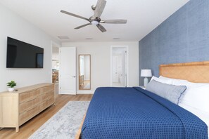 Une chambre à coucher avec un lit, une commode, un ventilateur de plafond et un téléviseur fixé au mur.