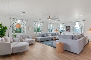 Uma sala de estar espaçosa com um amplo sofá modular cinzento, uma poltrona cinza e uma mesa lateral redonda de madeira.