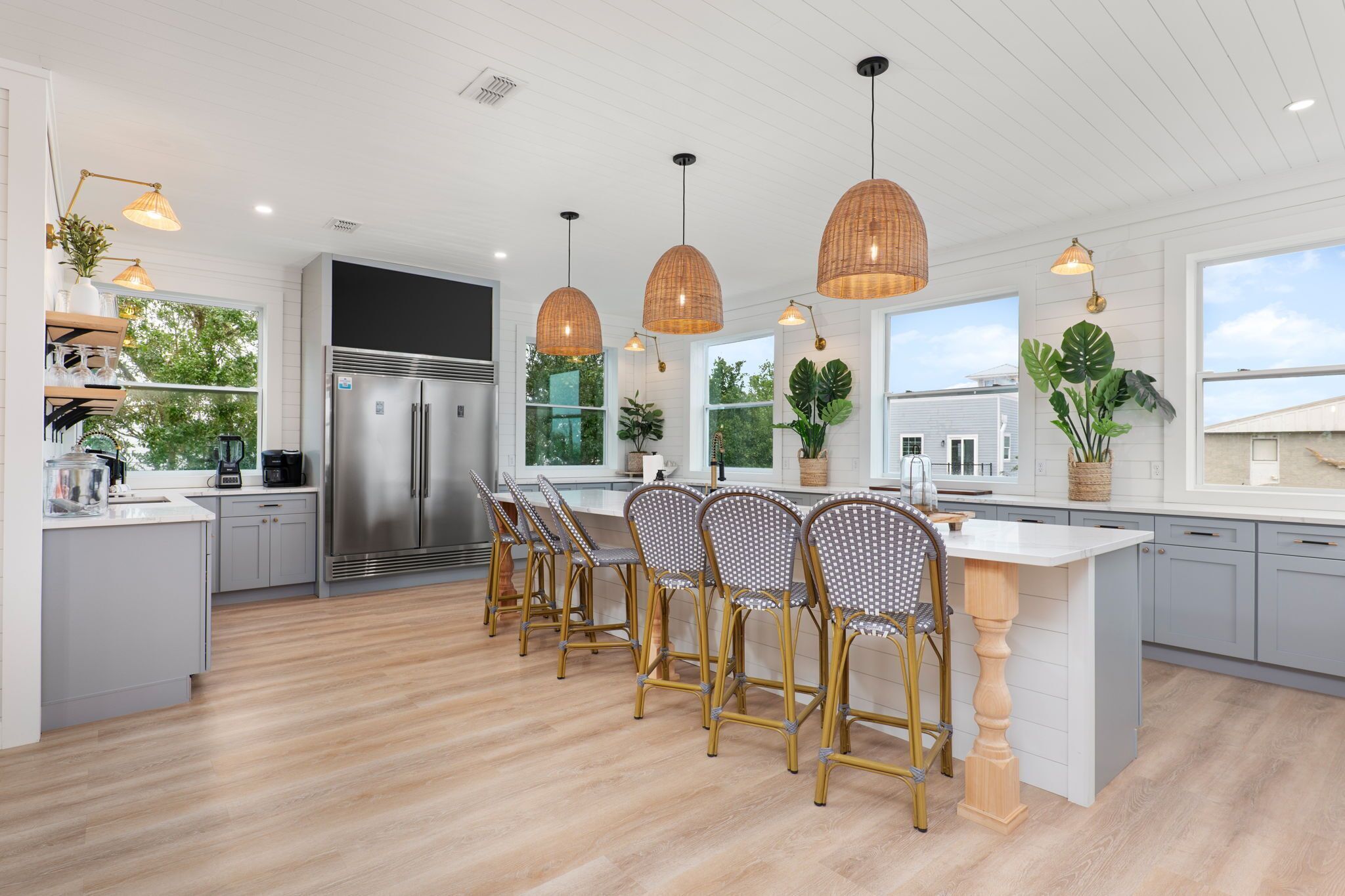 A modern kitchen with a central island, bar stools, pendant lighting, and large windows.