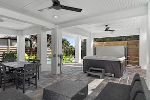 Eine überdachte Terrasse im Freien mit Esstisch, Stühlen, einem Whirlpool und einem Deckenventilator.
