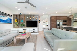 A modern living room with a flat-screen TV, sofas, a coffee table, and a kitchen area with appliances. - 8 bedrooms, Sleeps 18, 2 Golf Carts, Heated Pool, Swim Spa, Hot Tub, Paddle Boards, Rooftop Deck (St. Augustine)