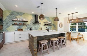 A modern kitchen with a large island, bar stools, and a view of the outdoors. - 8 bedrooms, Sleeps 18, 2 Golf Carts, Heated Pool, Swim Spa, Hot Tub, Paddle Boards, Rooftop Deck (St. Augustine)