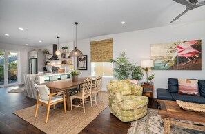 A modern kitchen with a marble island, dining area with wooden chairs, a sofa with a tropical print, and a large painting of a flamingo. - 8 bedrooms, Sleeps 18, 2 Golf Carts, Heated Pool, Swim Spa, Hot Tub, Paddle Boards, Rooftop Deck (St. Augustine)