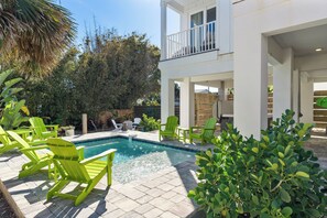 A pool area with green chairs, a two-story building, and surrounding greenery. - 8 bedrooms, Sleeps 18, 2 Golf Carts, Heated Pool, Swim Spa, Hot Tub, Paddle Boards, Rooftop Deck (St. Augustine)