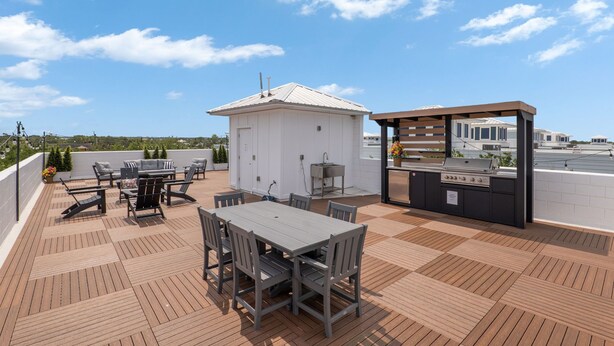 Terraza en la azotea con mesa, sillas, una parrilla y un pequeño edificio blanco.