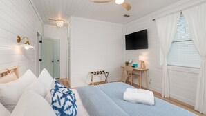 Un dormitorio con cama, escritorio, silla, televisor y ventilador de techo.