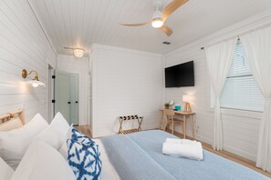 Ein Schlafzimmer mit Bett, Schreibtisch, Stuhl, Fernseher und Deckenventilator.