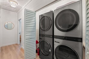 A laundry room with two stacked front-loading washing machines, a mirror, and a door with horizontal slats. - Osprey Nest - Rooftop/Pool/Water Views (St. Augustine)