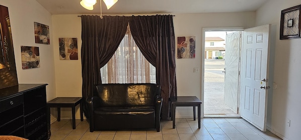 A room with a black leather sofa, a small table, a cabinet, and a door leading outside.