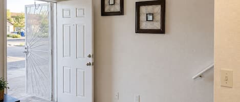 A hallway with a white door, two wall-mounted picture frames, a light switch, and a power outlet.