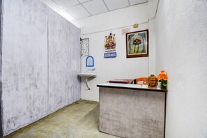 A small, enclosed room with a white sink, a small desk with a Buddha statue, and religious posters on the wall.