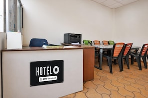 A hotel reception desk with a sign indicating it is serviced by OYO. There is a printer, a blue chair, and a table with colorful chairs. - Deluxe Sea Bird Resort (Kanthi)