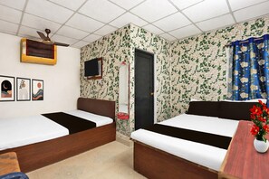 A room with two beds, a ceiling fan, a TV, and a window with curtains.