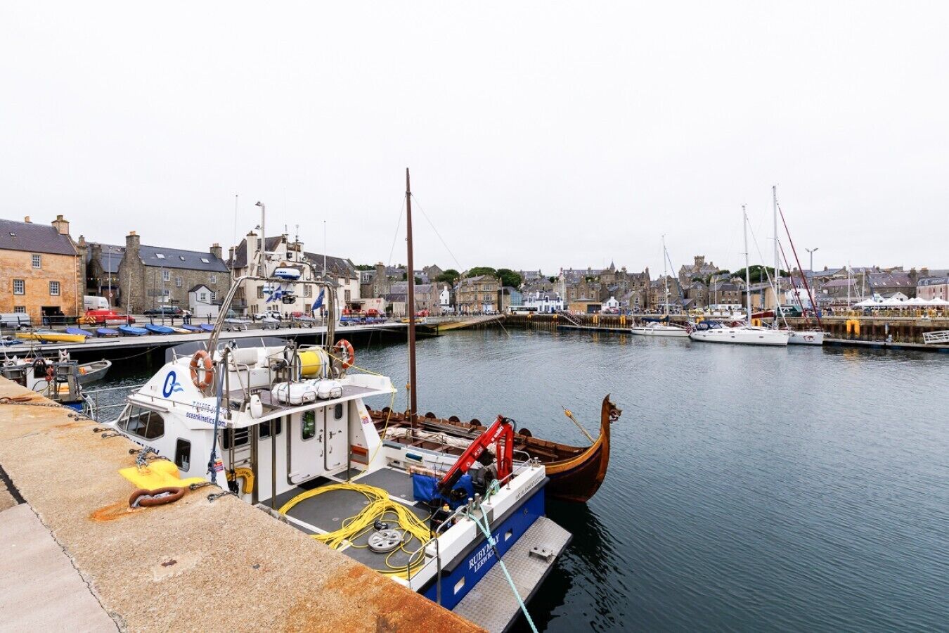 A harbor with boats docked, a wooden boat with a dragon head, and buildings in the background.