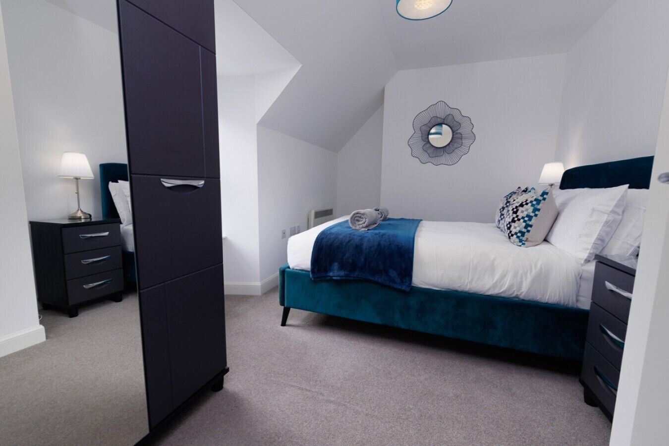 Un dormitorio con cama, armario, mesita de noche y espejo instalado en la pared.