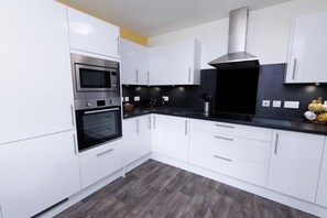 A modern kitchen with white cabinets, a black countertop, stainless steel appliances, and a grey floor. - Central Lerwick House, Modern, 2 Bathrooms, Garden (Lerwick)
