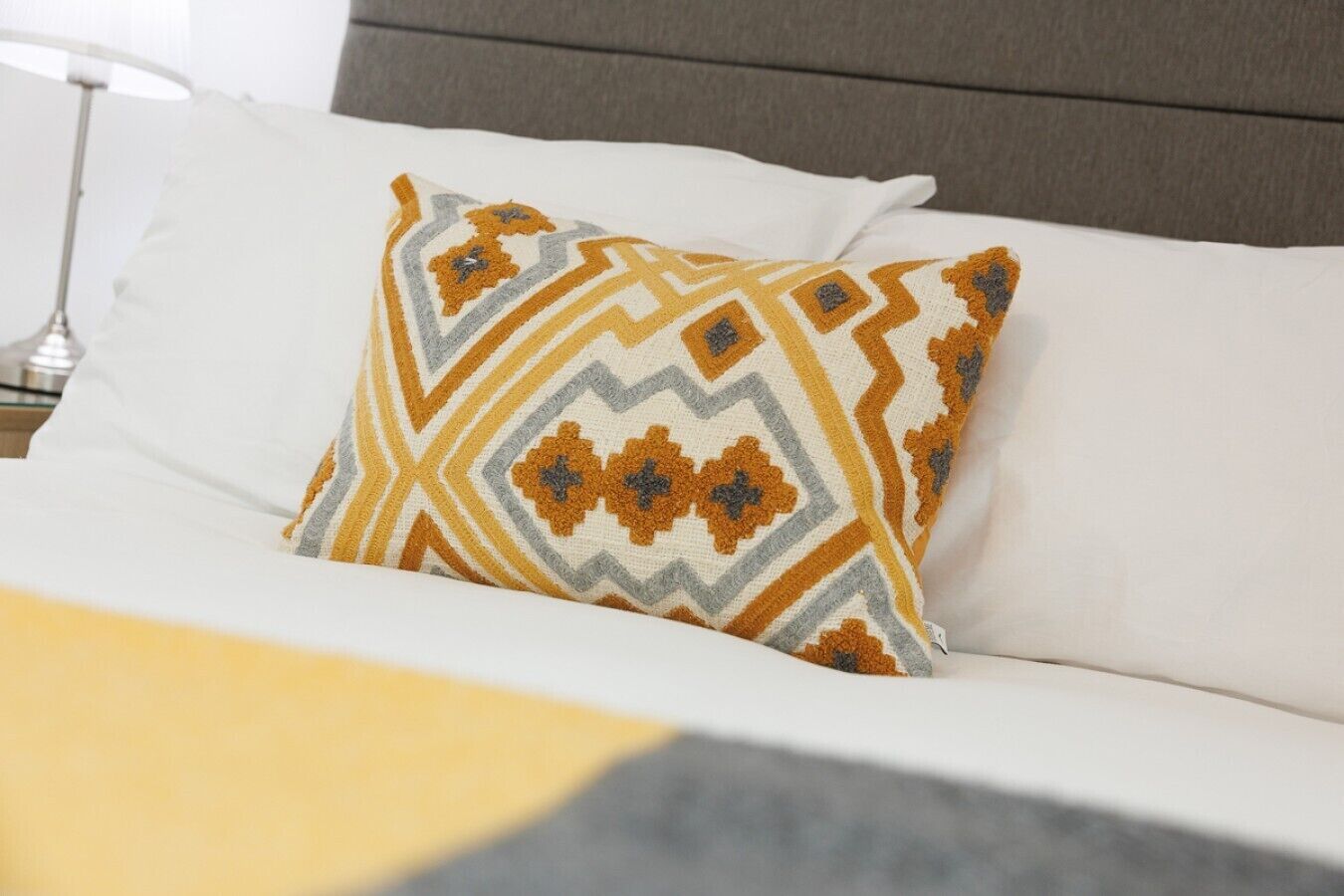A bed with a patterned pillow and a plain white pillow.