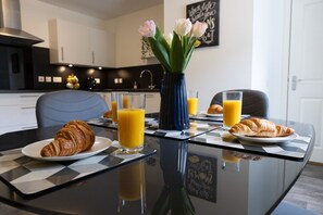 A breakfast setting with croissants, orange juice, and a vase of flowers on a glass table.