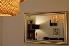 A room with a large mirror, a floor lamp, a small plant, and a framed picture on the wall.