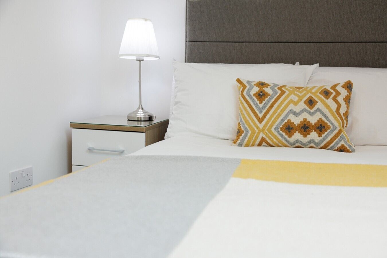 A neatly made bed with a patterned pillow, a bedside lamp, and a nightstand with a drawer.